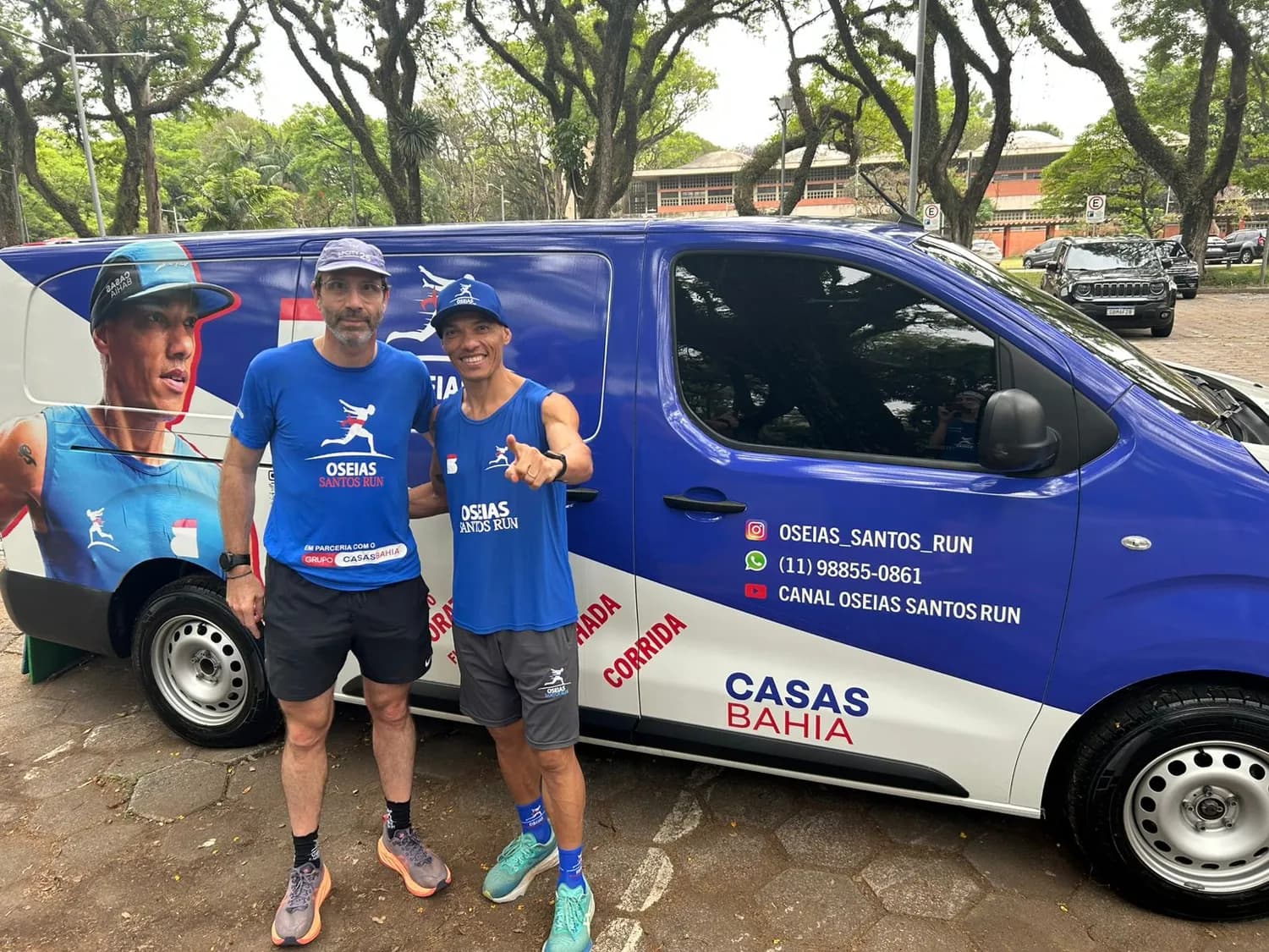 Oseias e um atleta da equipe ao lado da van adesivada com a marca do Grupo Casas Bahia